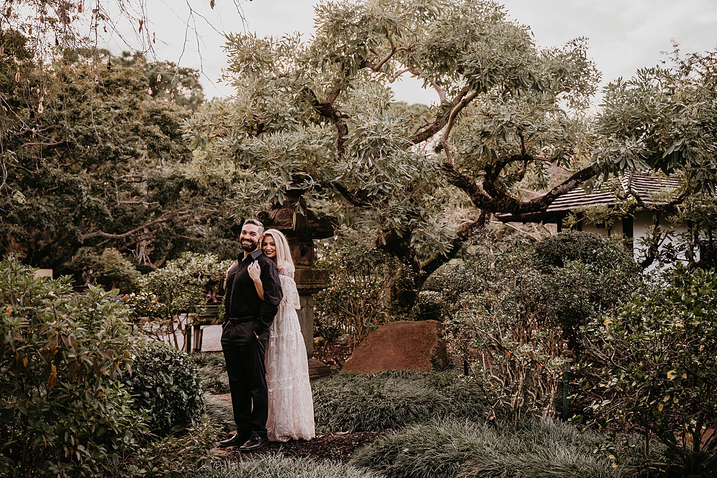Woman holding man from behind with green trees Morikami Museum and Japanese Gardens Engagement Photography captured by Krystal Capone Photography