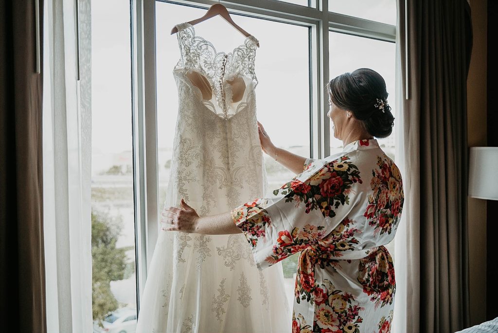 Bride looking at her dress hanging on top of sliding glass door 94th Aero Squadron Miami Wedding Photography captured by South Florida Engagement Photographer Krystal Capone Photography 