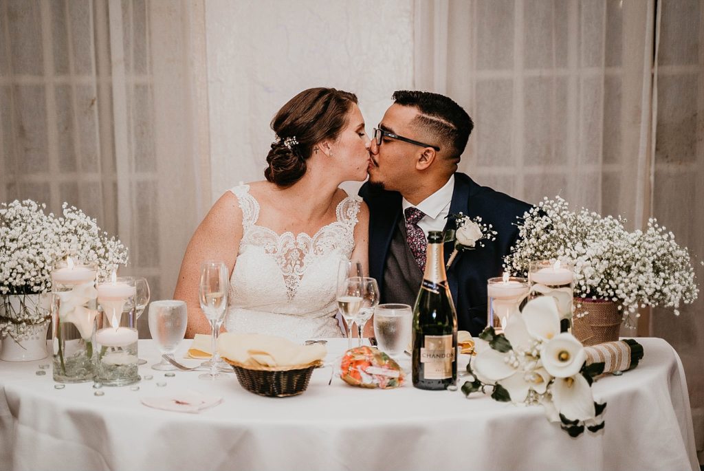 Bride and Groom kissing at sweetheart table 94th Aero Squadron Miami Wedding Photography captured by South Florida Engagement Photographer Krystal Capone Photography 