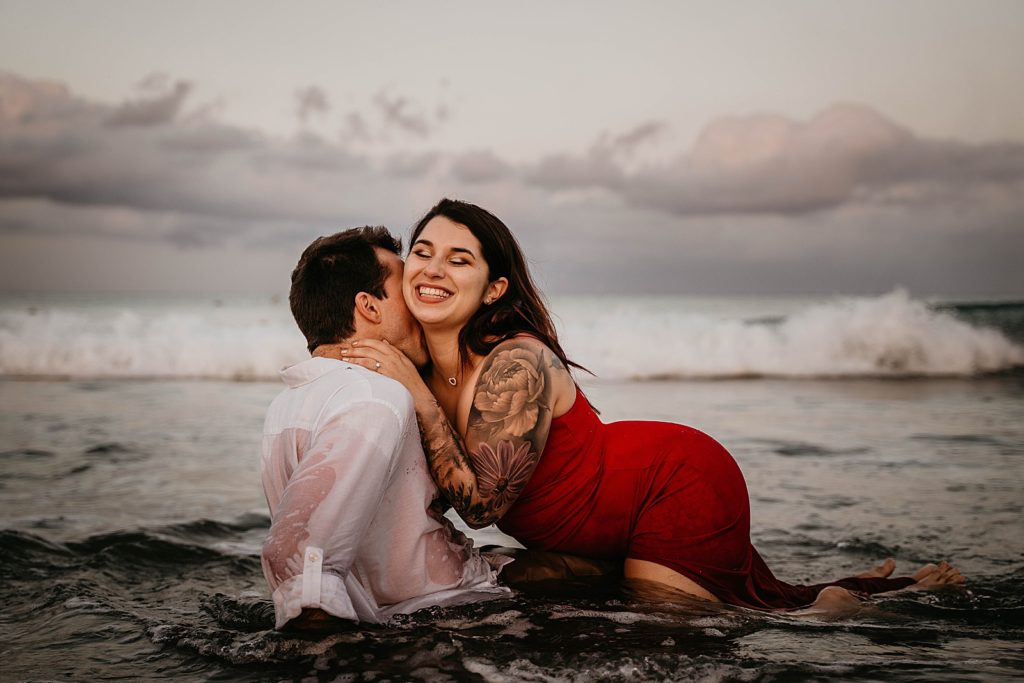 Couple laughing and smiling as they drift into shallow ocean water on the beach Palm Beach Engagement Photography captured by South Florida Engagement Photographer Krystal Capone Photography 