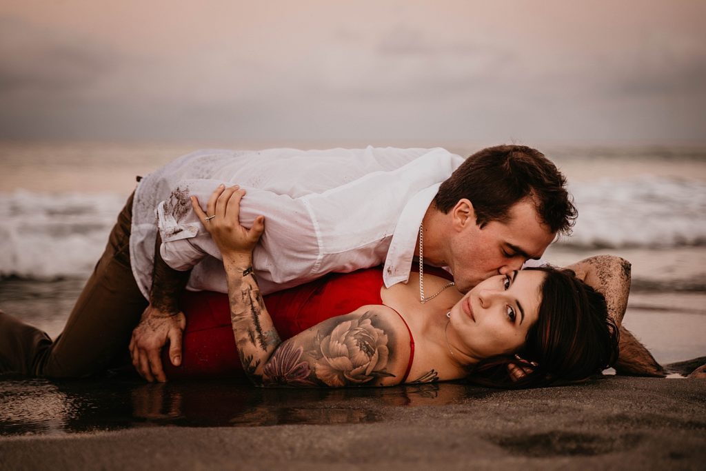 Man kisses woman lying on the wet sand of the beach Palm Beach Engagement Photography captured by South Florida Engagement Photographer Krystal Capone Photography 