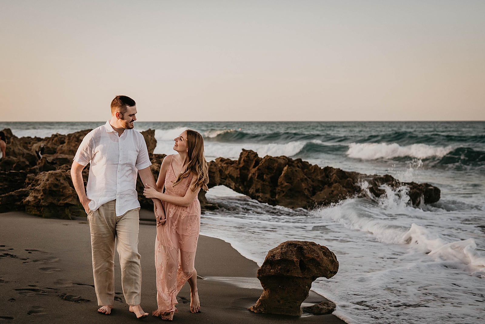 Couple walking along crashing waves on the wet sand of the beach