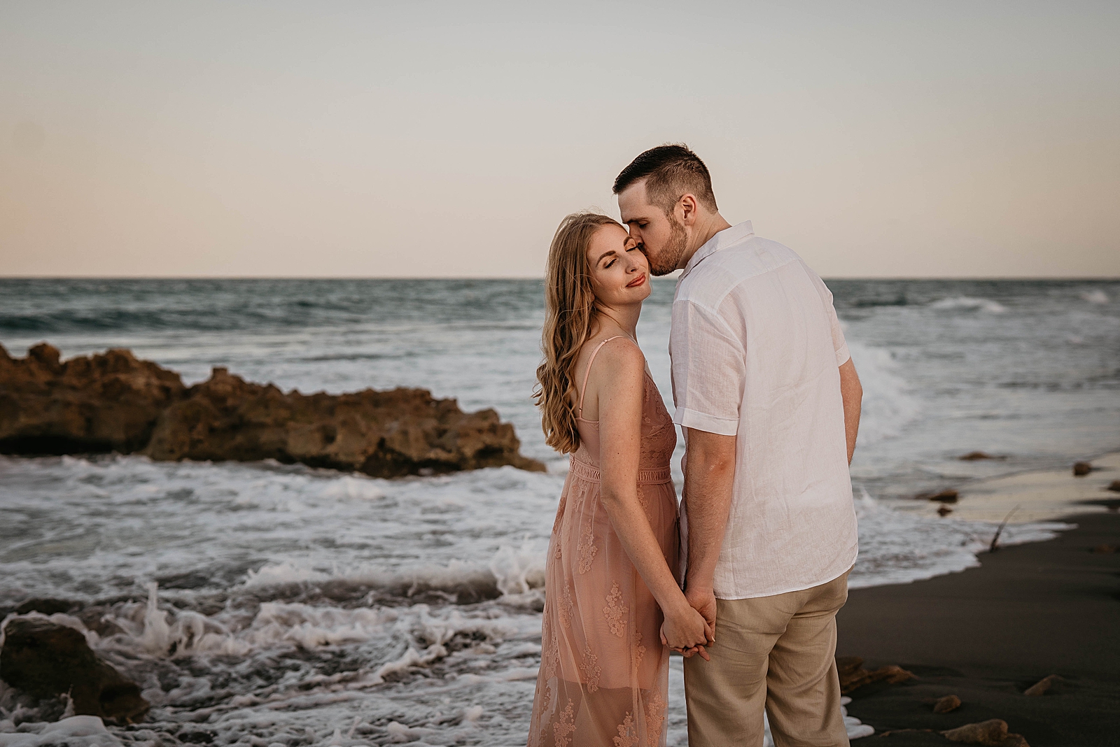 Man kissing woman on the cheek by the ocean on the beach