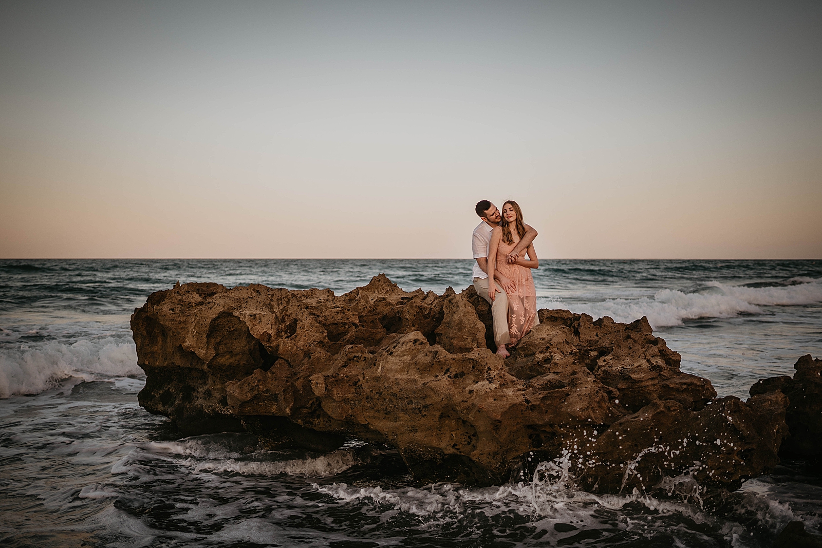 Couple sitting on large drift rock on the beach