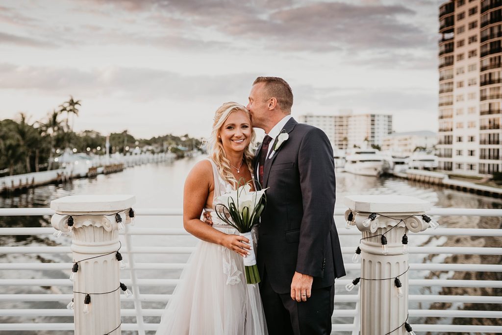 Groom kissing Bride on the side of the head by the water