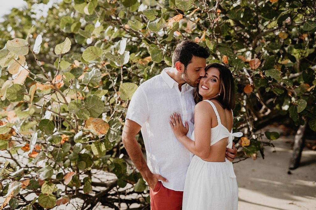 Man kissing woman on the cheek by greenery