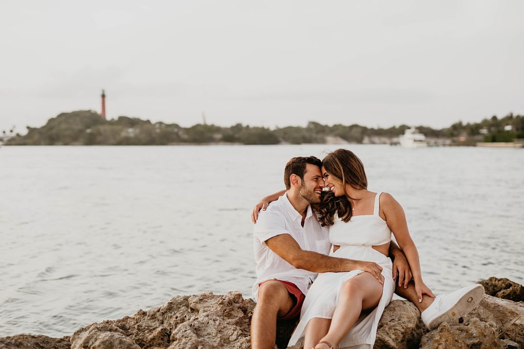 Couple sitting on rocks with the lighthouse in the distance