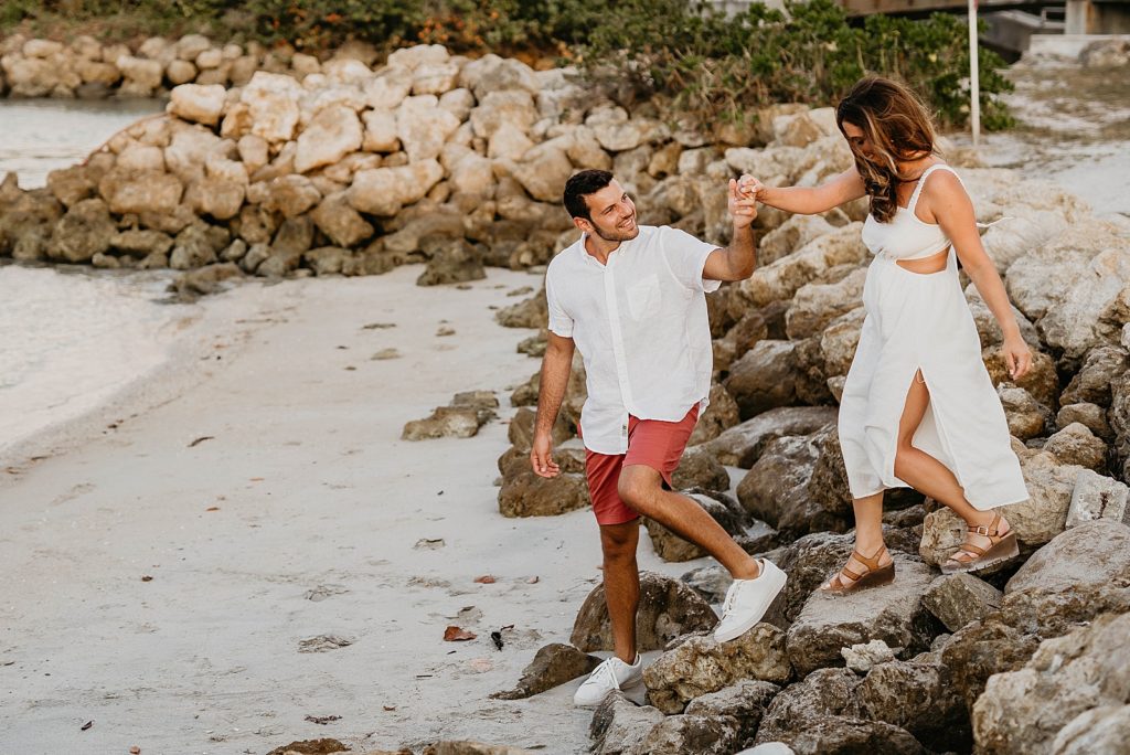 Couple walking down rocks on the beach holding hands