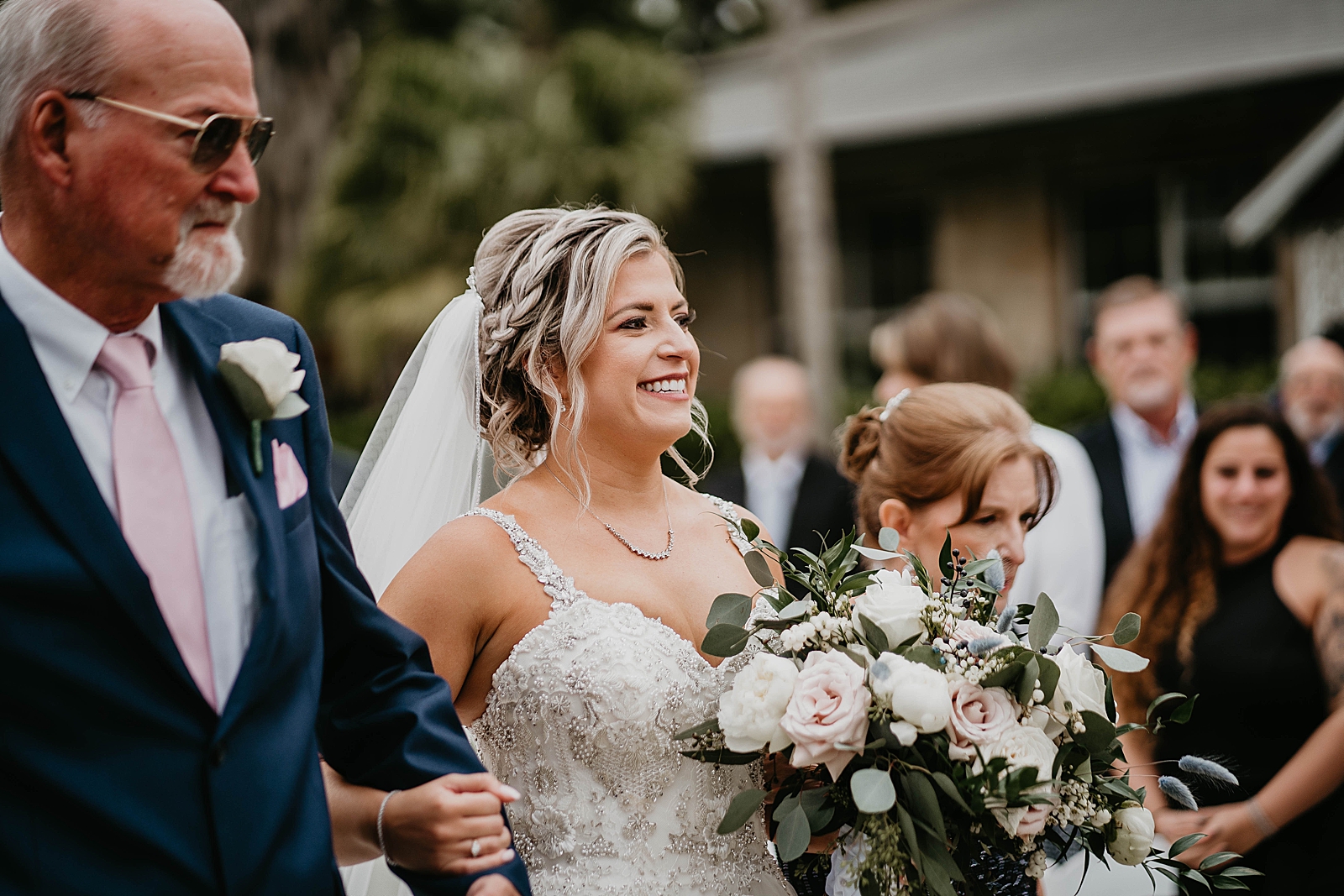 Bride with her arm around father's arm and mother next to her entering Ceremony
