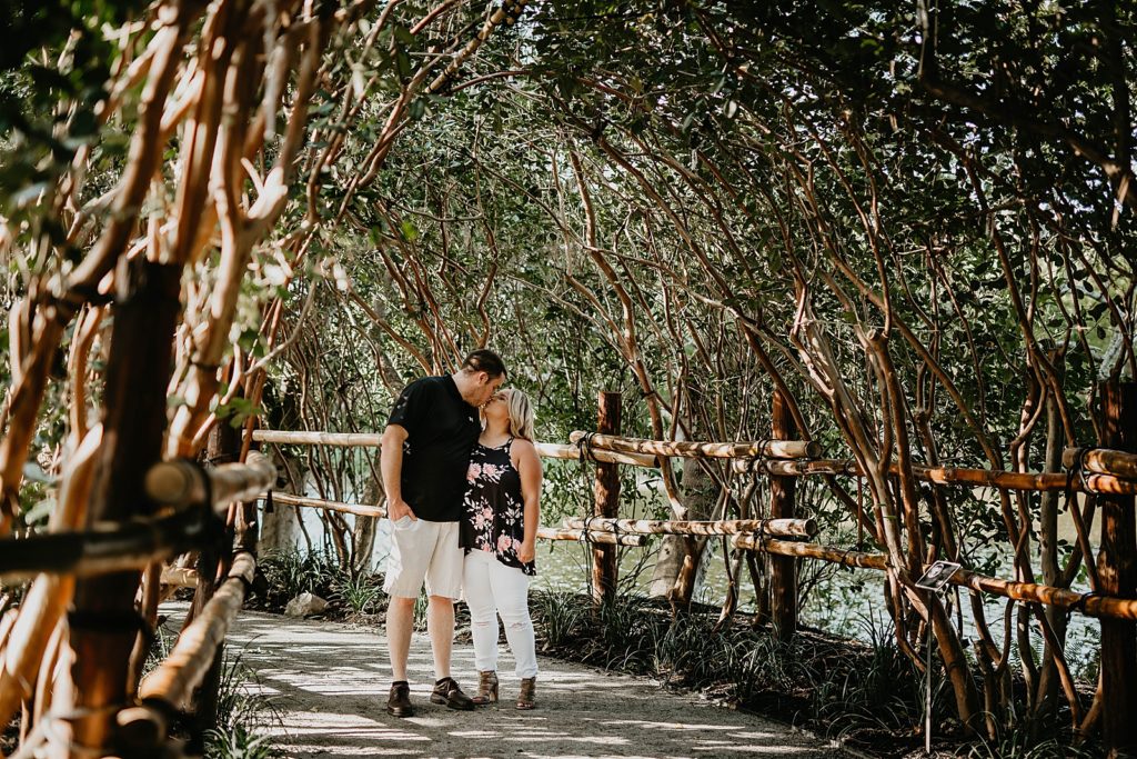 Couple kissing under natural tree arch and wooden fence