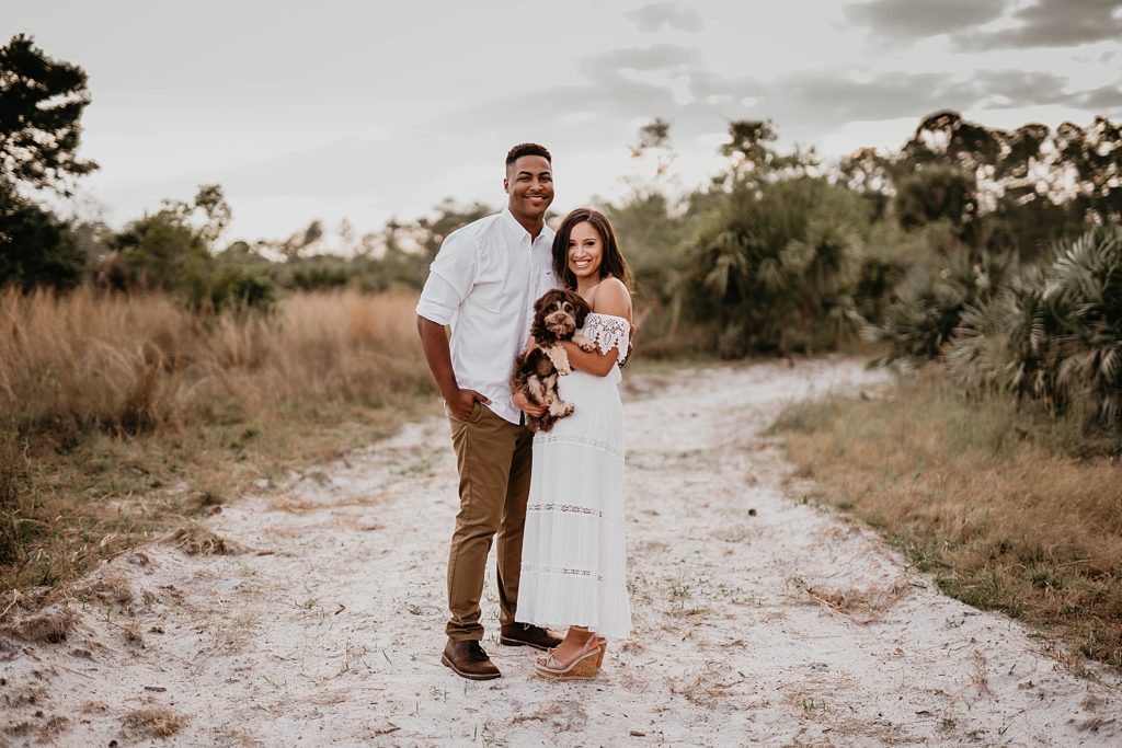 Couple posing holding their dog on sand path