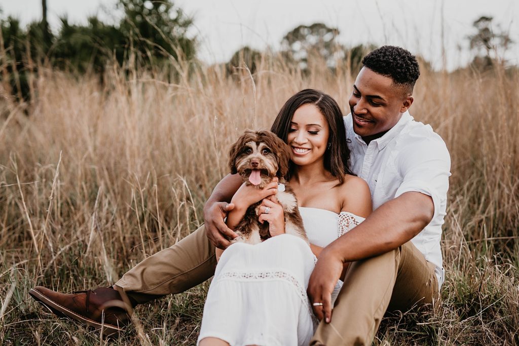 Couple sitting in tall grass with their dog