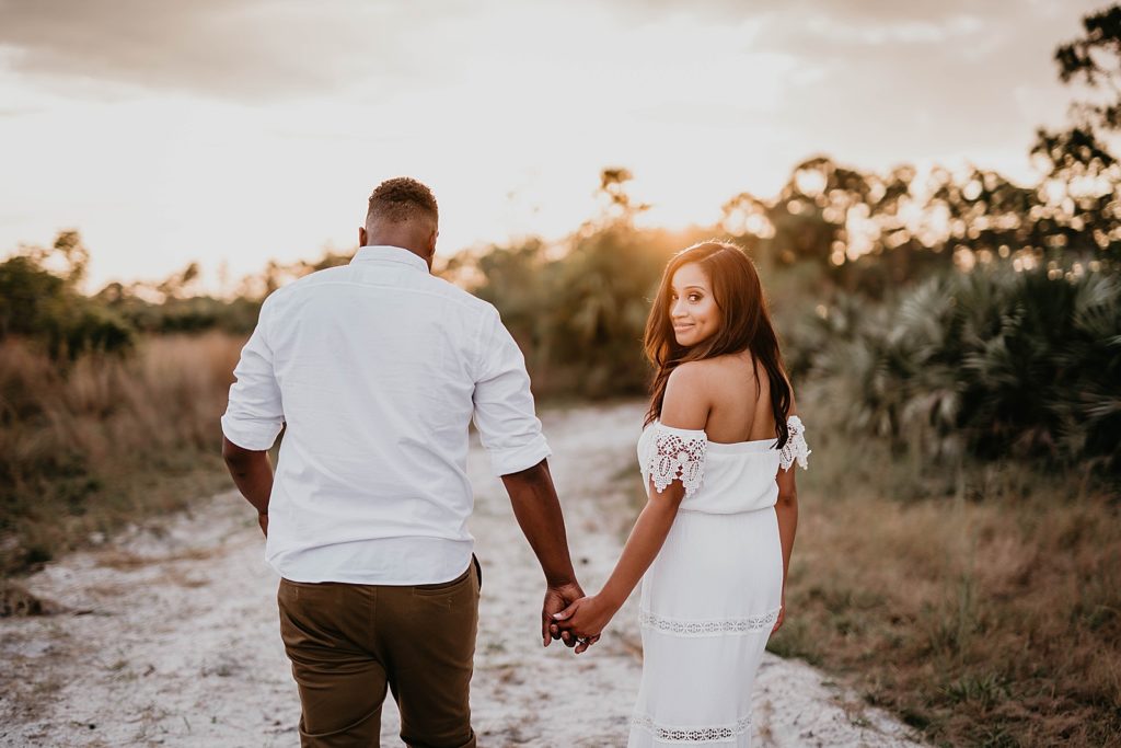Couple holding hands walking on sand path with the sun setting