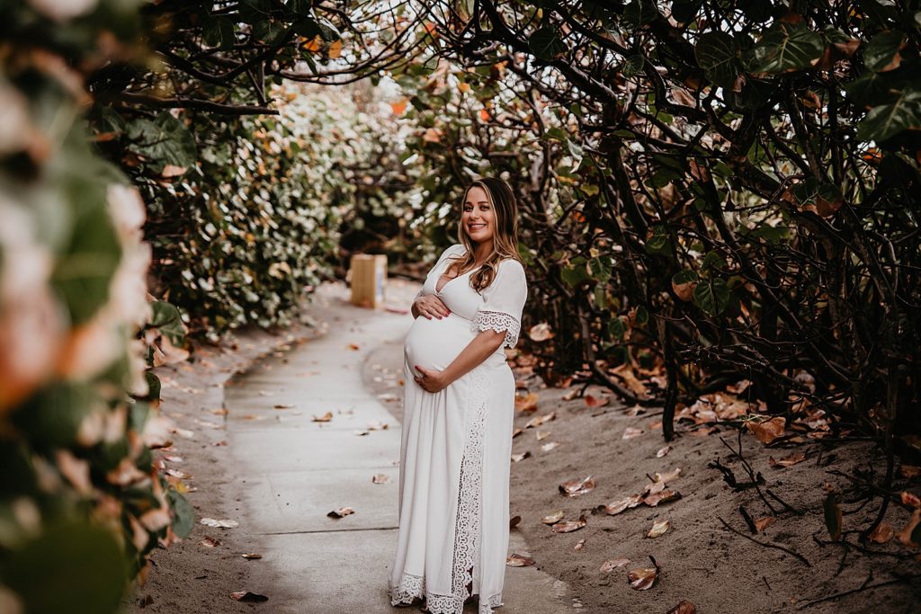 Pregnant woman standing on beach sidewalk and holding her baby bump