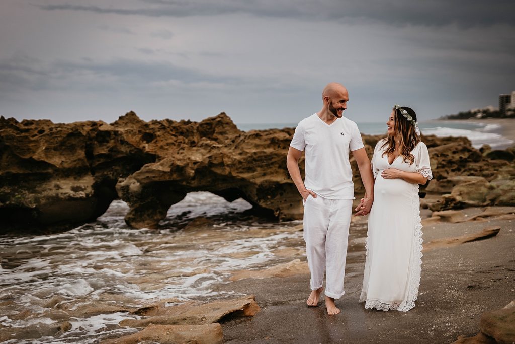Pregnant couple holding hands and walking on the beach together