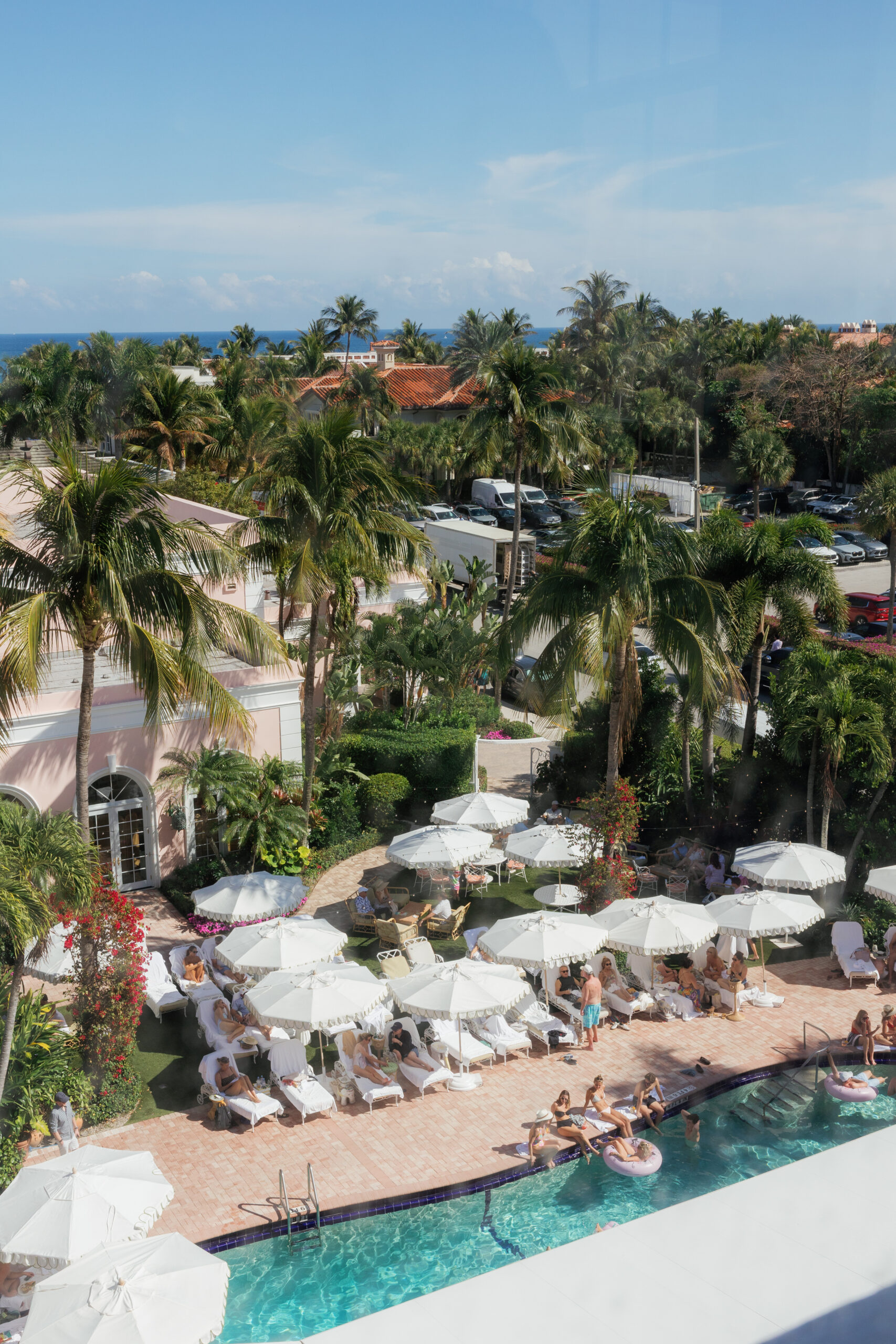 Harper and Luke wedding at The Colony Palm Beach - cocktail hour - An aerial view of guests relaxing by a swimming pool with lounge chairs and umbr