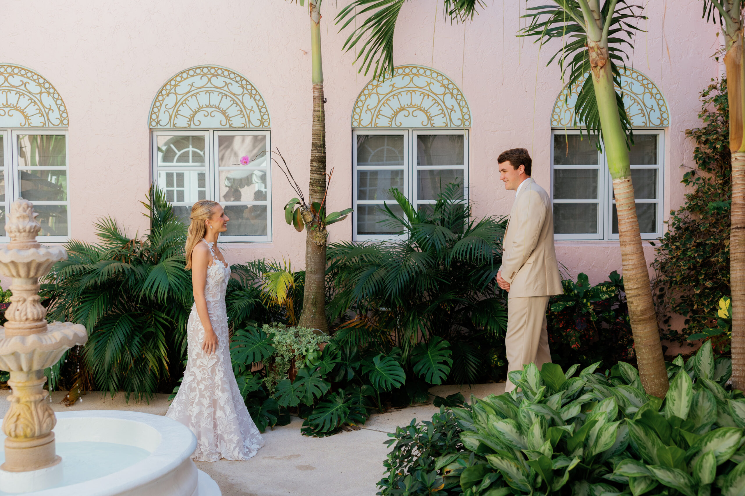 Harper and Luke wedding at The Colony Palm Beach - getting ready - The bride and groom are having a first look in a lush garden with a pink buildin