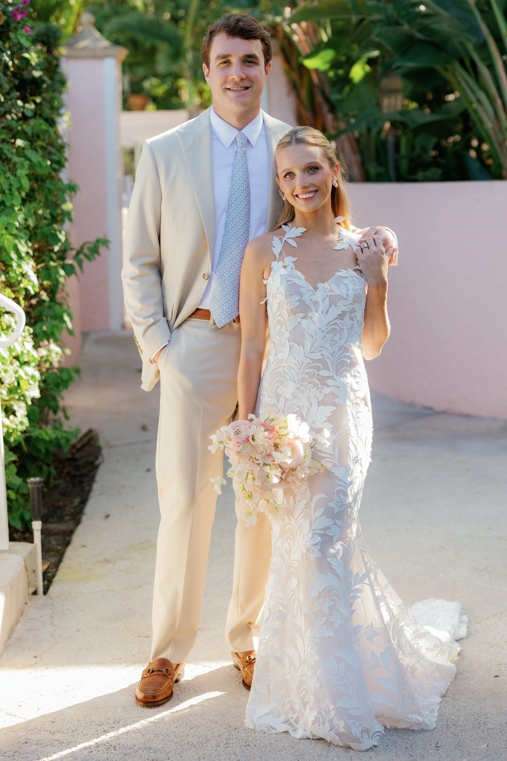 Harper and Luke wedding at The Colony Palm Beach - getting ready - A bride in a white lace dress and a groom in a beige suit pose together outdoors