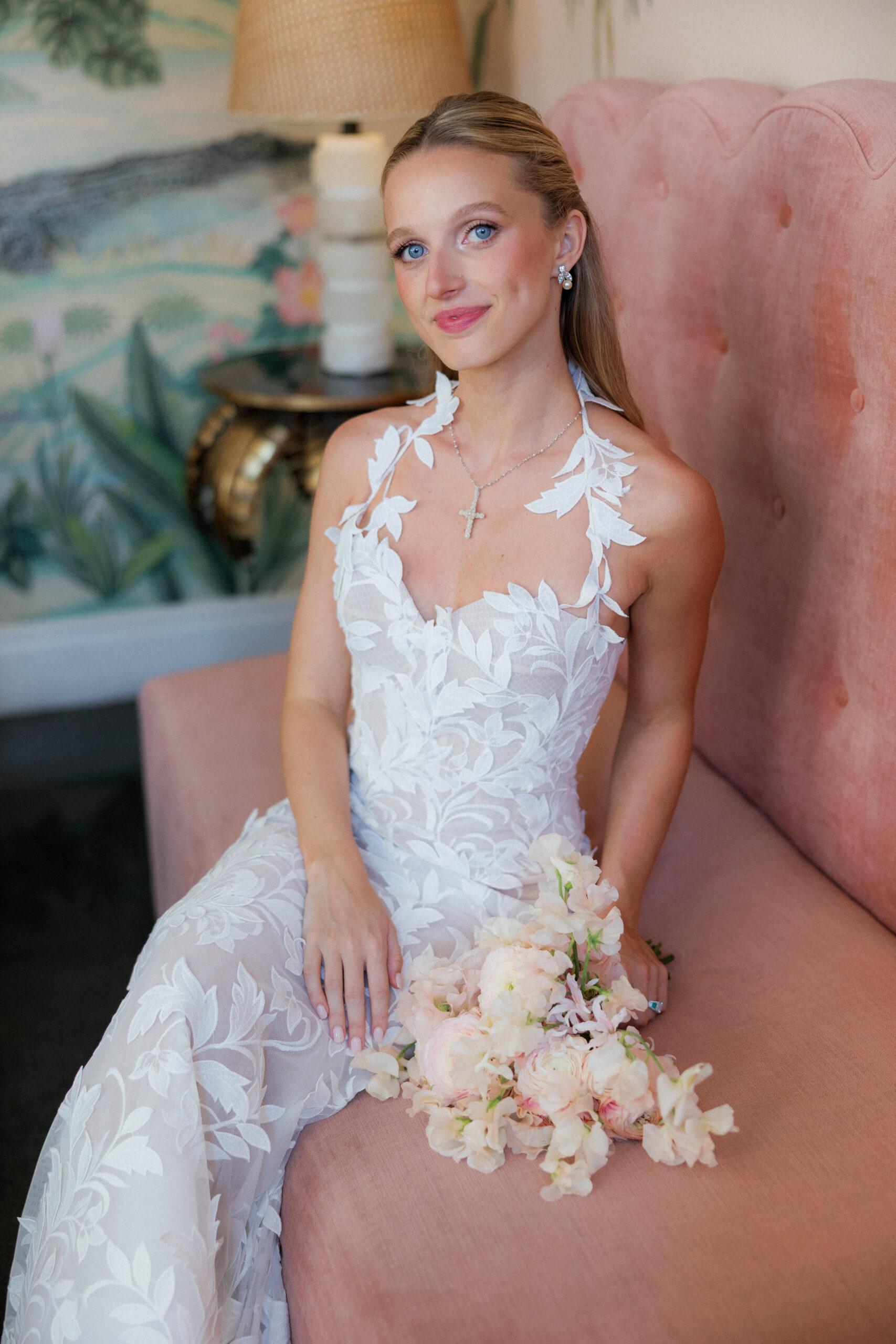 Harper and Luke wedding at The Colony Palm Beach - getting ready - A bride in a white wedding dress sits on a pink couch, holding a light pink and 