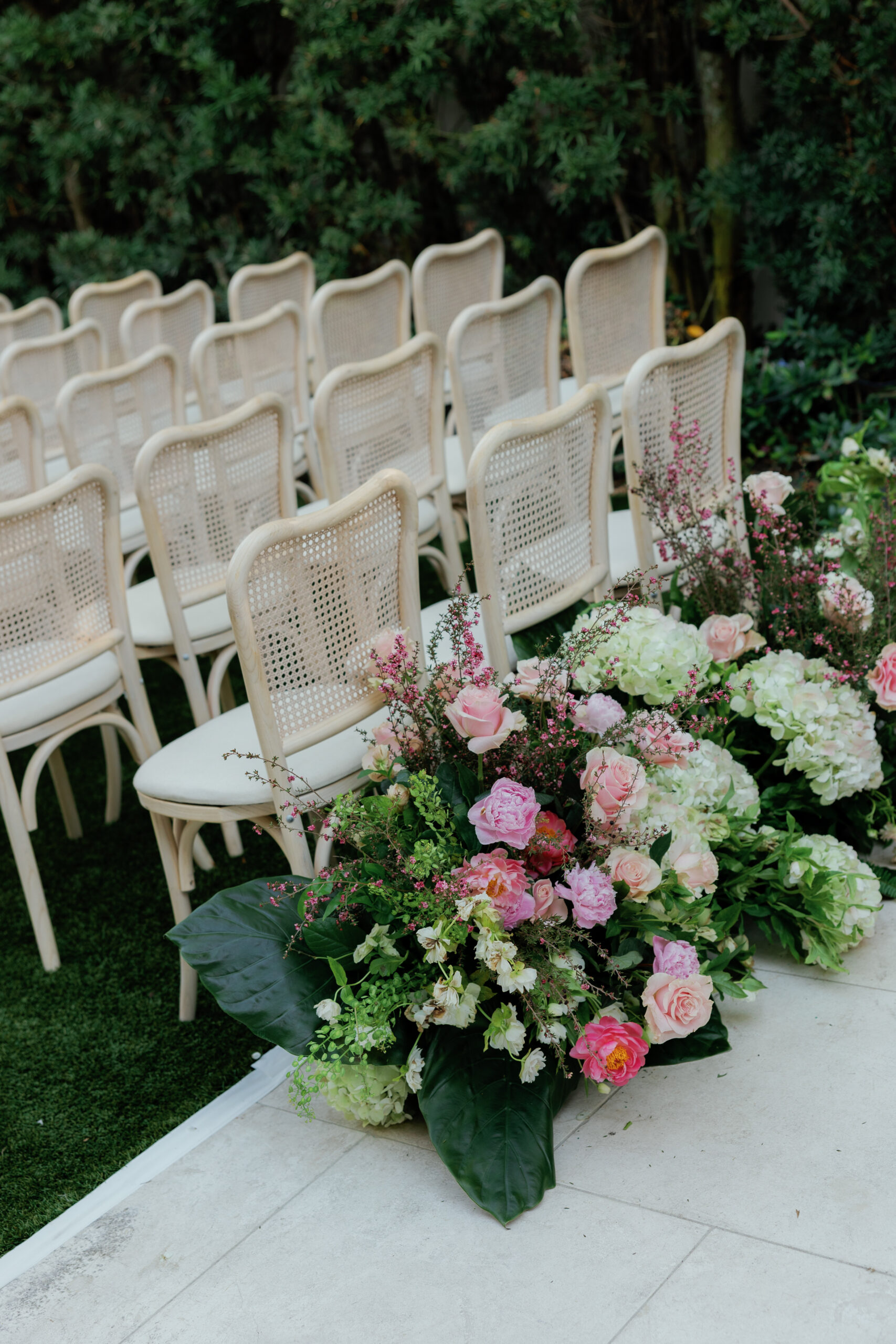 Harper and Luke wedding at The Colony Palm Beach - ceremony - Rows of white chairs are set up outdoors with floral arrangements lining an aisl