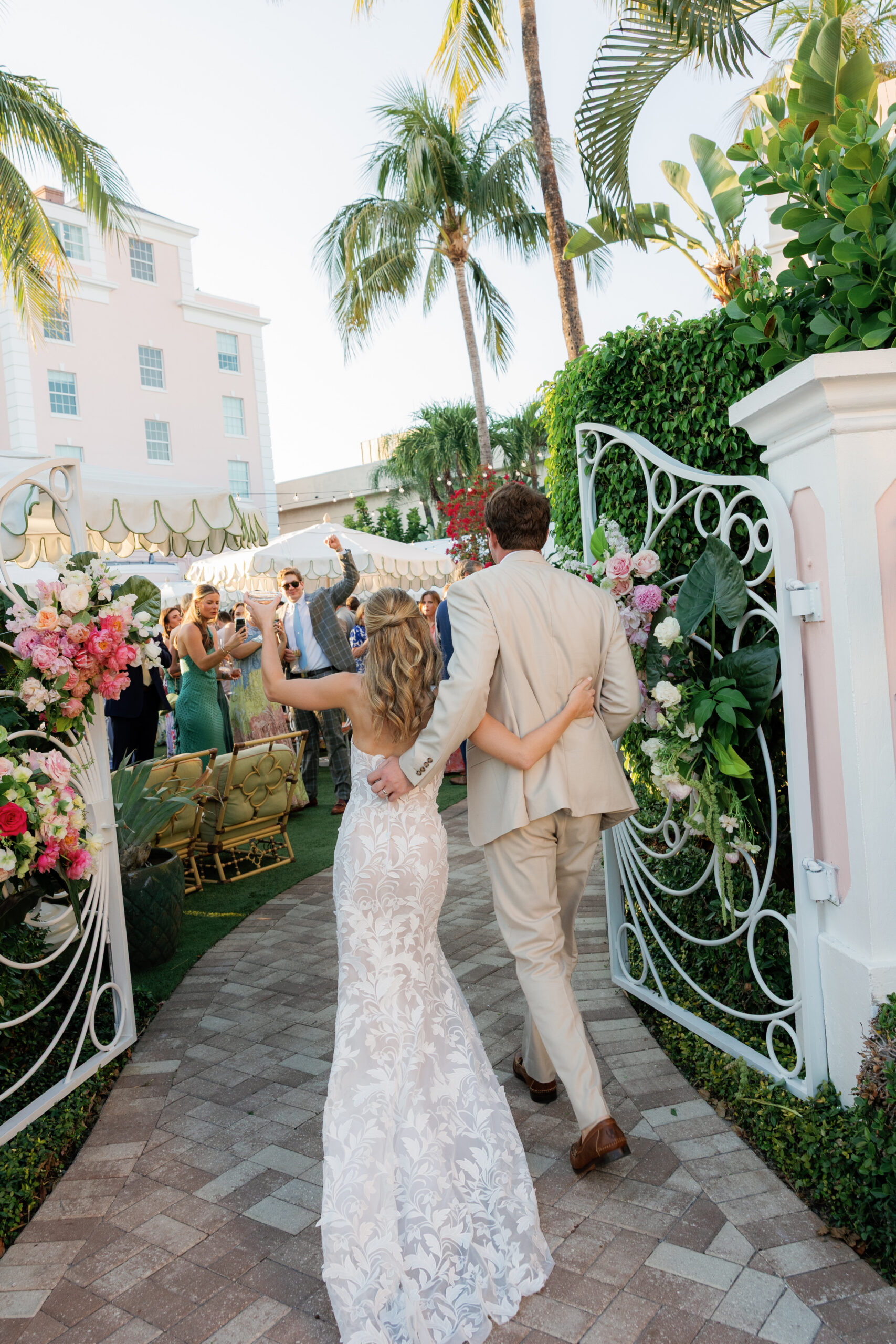 Harper and Luke wedding at The Colony Palm Beach - cocktail hour - A newlywed couple walks through an ornate gate, cheered on by guests in an outdo