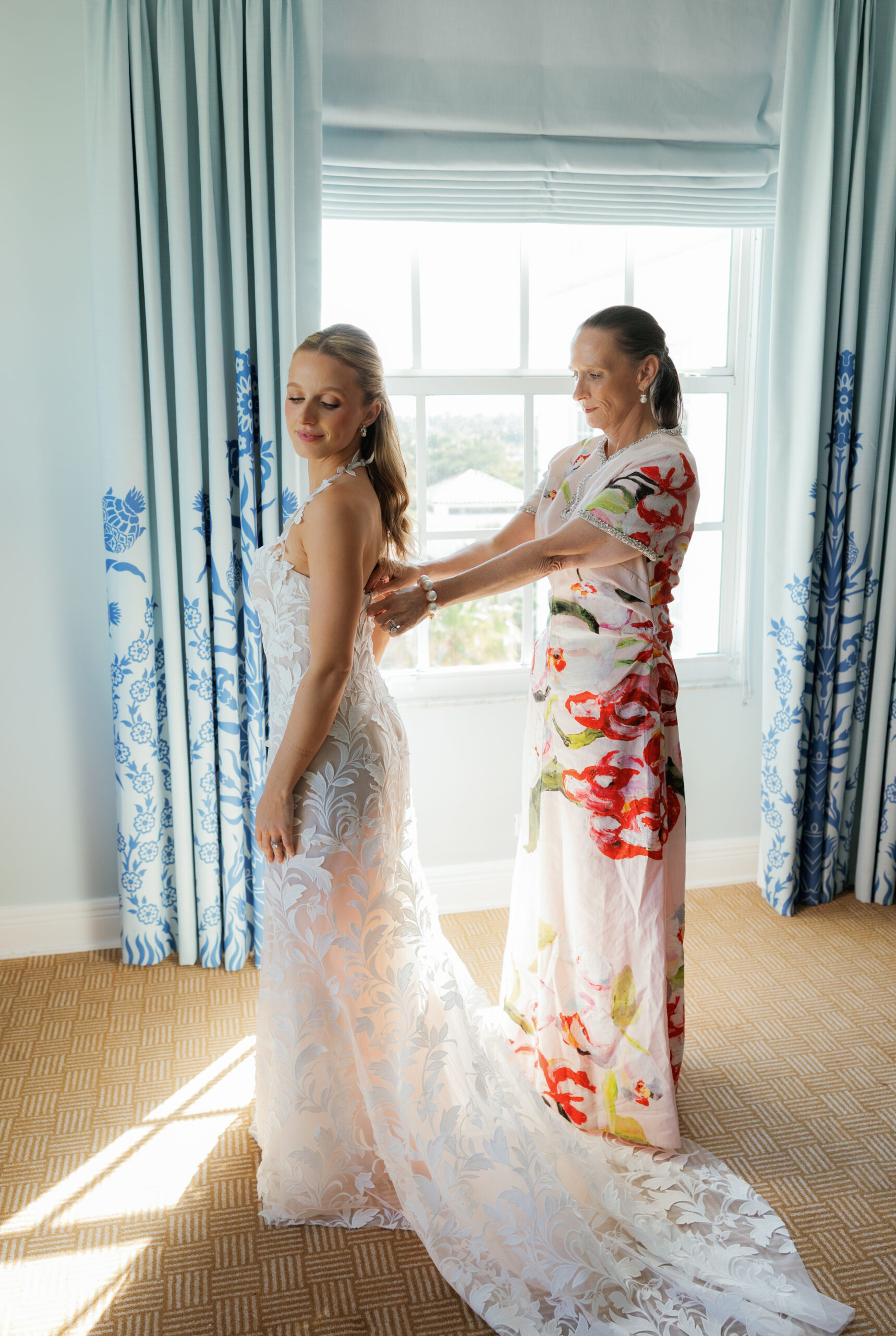 Harper and Luke wedding at The Colony Palm Beach - getting ready - A bride is being helped into her white wedding dress by another woman in a room 