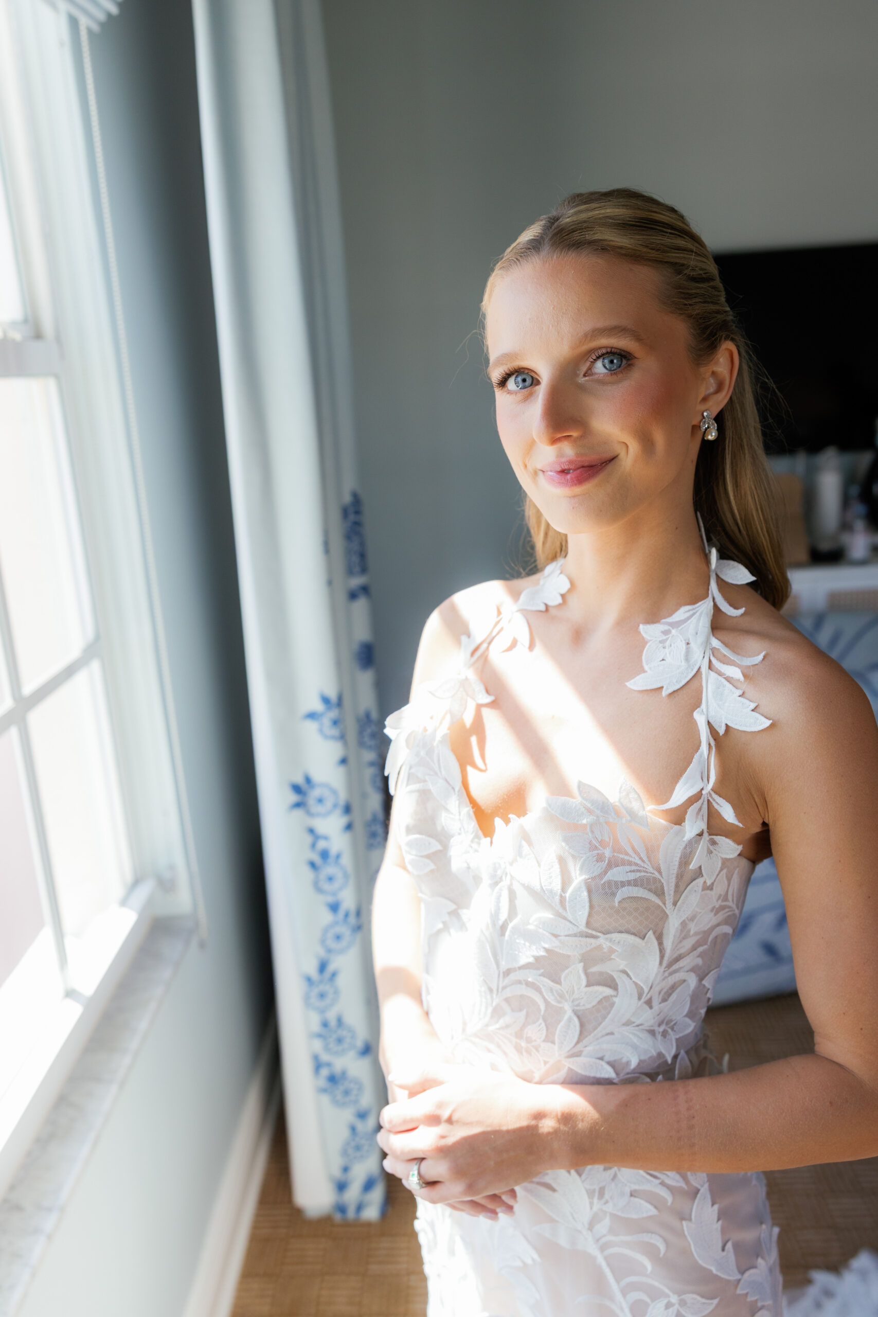 Harper and Luke wedding at The Colony Palm Beach - getting ready - A bride in a white dress stands by a window, bathed in sunlight, during her gett