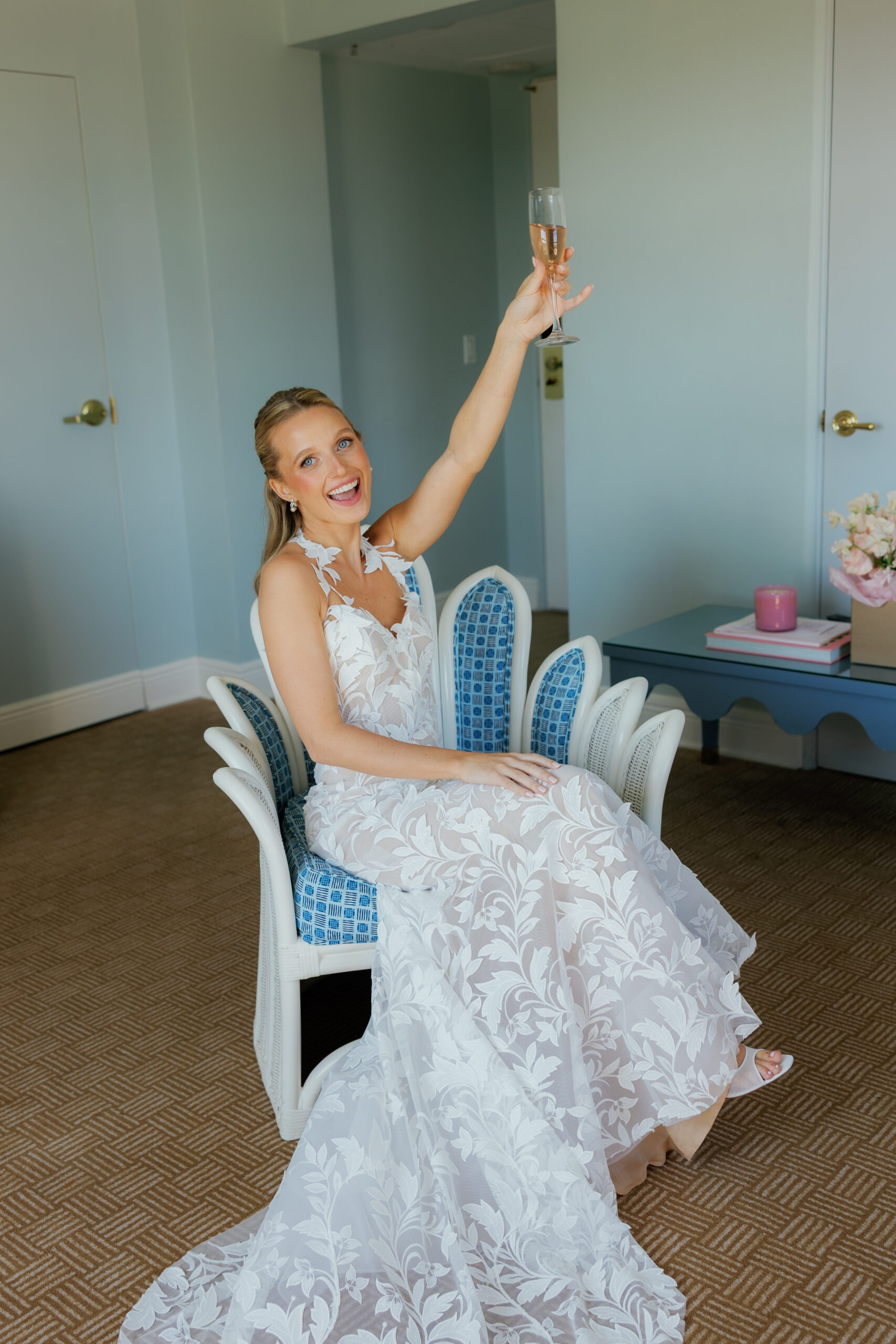 Harper and Luke wedding at The Colony Palm Beach - getting ready - A bride in her wedding dress raises a glass of champagne in a room.