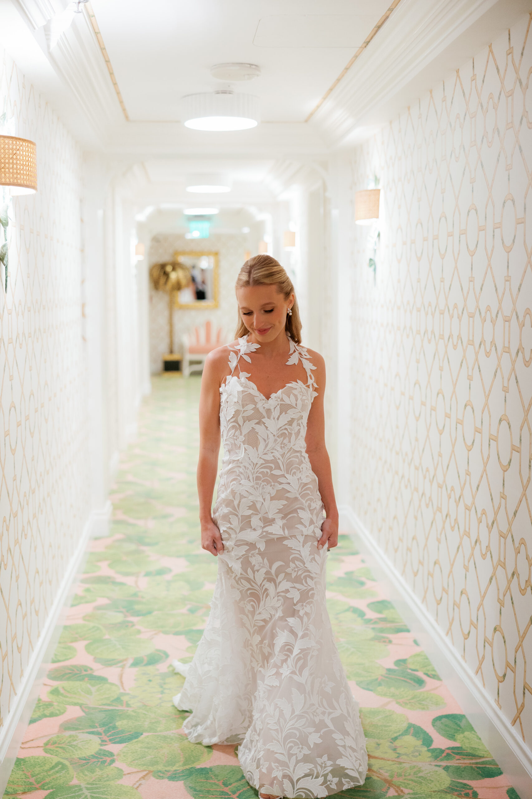 Harper and Luke wedding at The Colony Palm Beach - getting ready - A bride in a white wedding dress walks down a brightly lit hallway with patterne