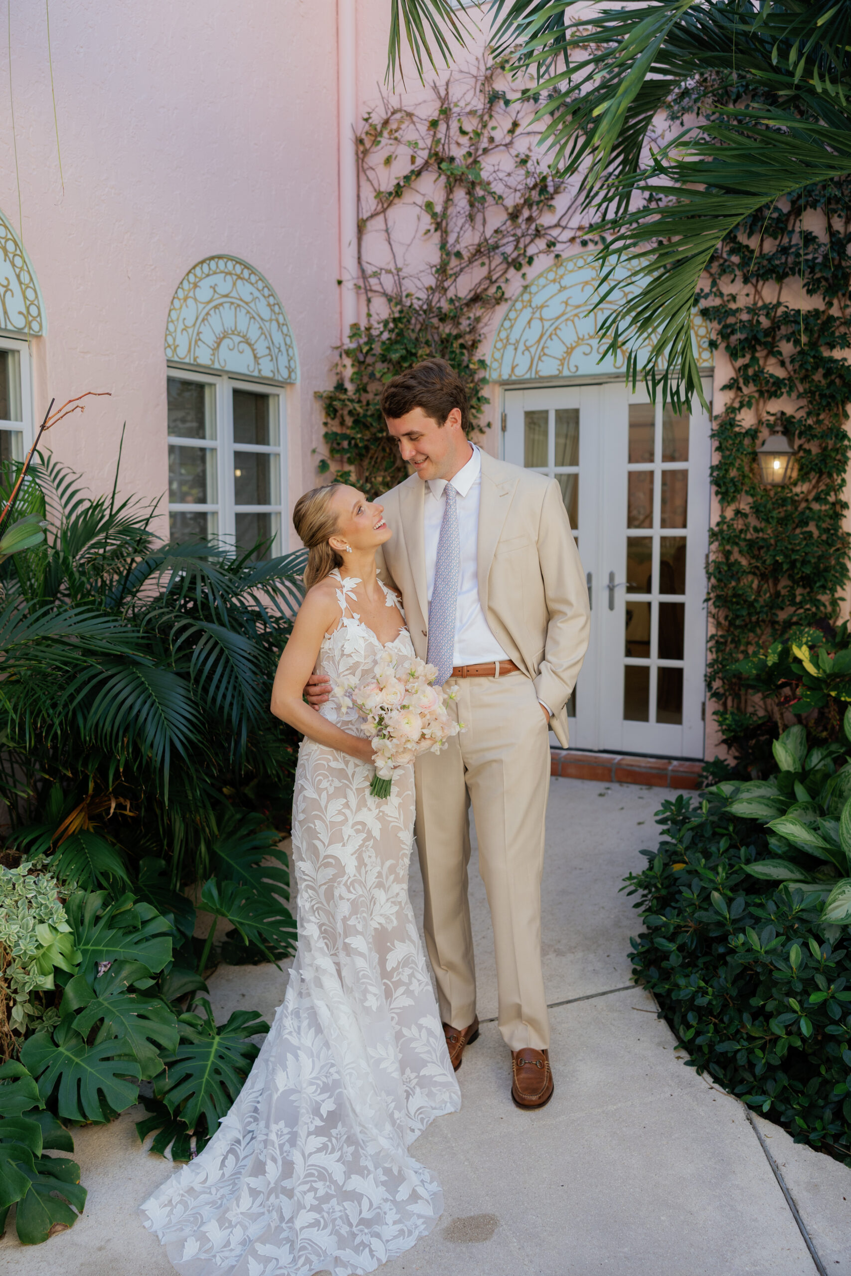 Harper and Luke wedding at The Colony Palm Beach - getting ready - The bride and groom pose together outdoors in front of a pink building with gree