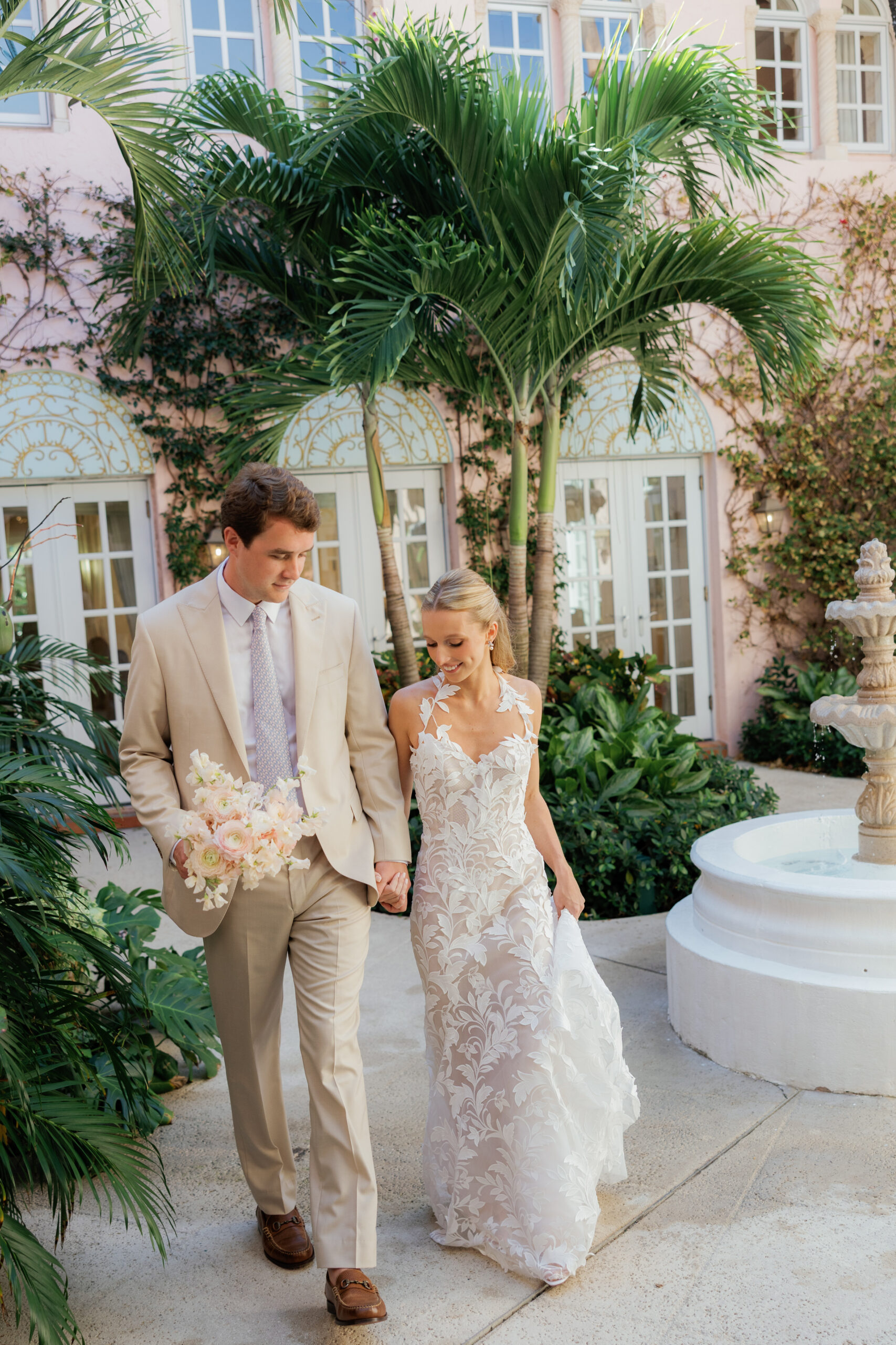 Harper and Luke wedding at The Colony Palm Beach - getting ready - The bride and groom walk hand-in-hand in a beautiful outdoor setting with palm t
