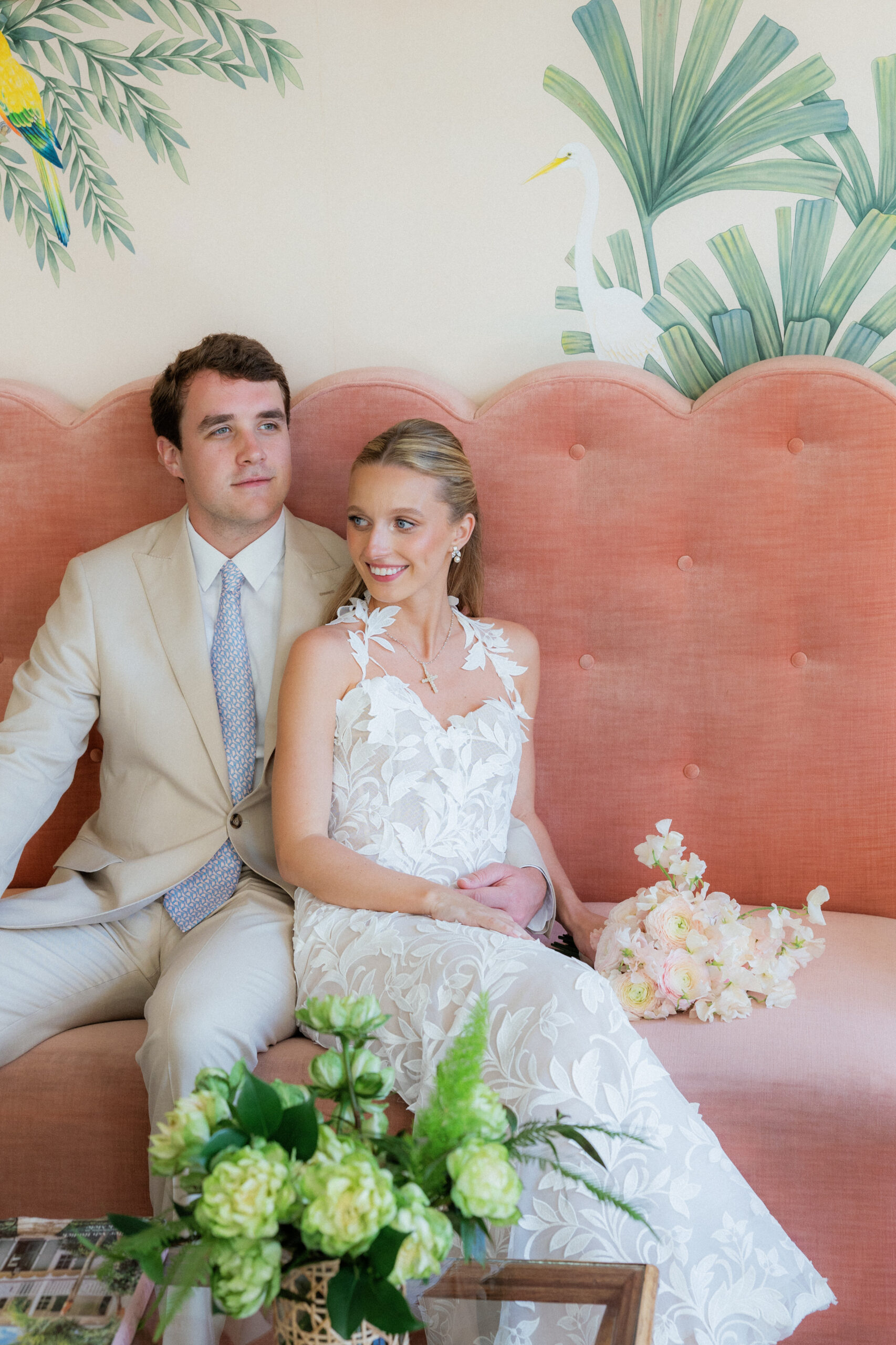 Harper and Luke wedding at The Colony Palm Beach - getting ready - A bride and groom are seated on a pink couch, posing for a portrait with flowers