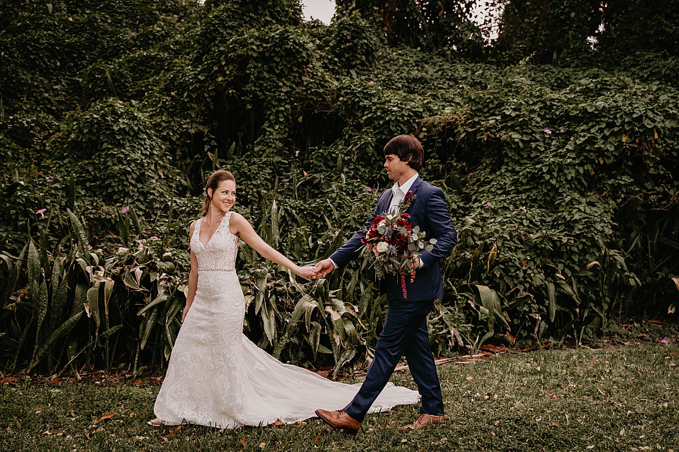 Bride holding Groom's hand leading him by greenery Out of the Blue Celebrations Wedding Photography captured by South Florida Wedding Photographer Krystal Capone Photography 