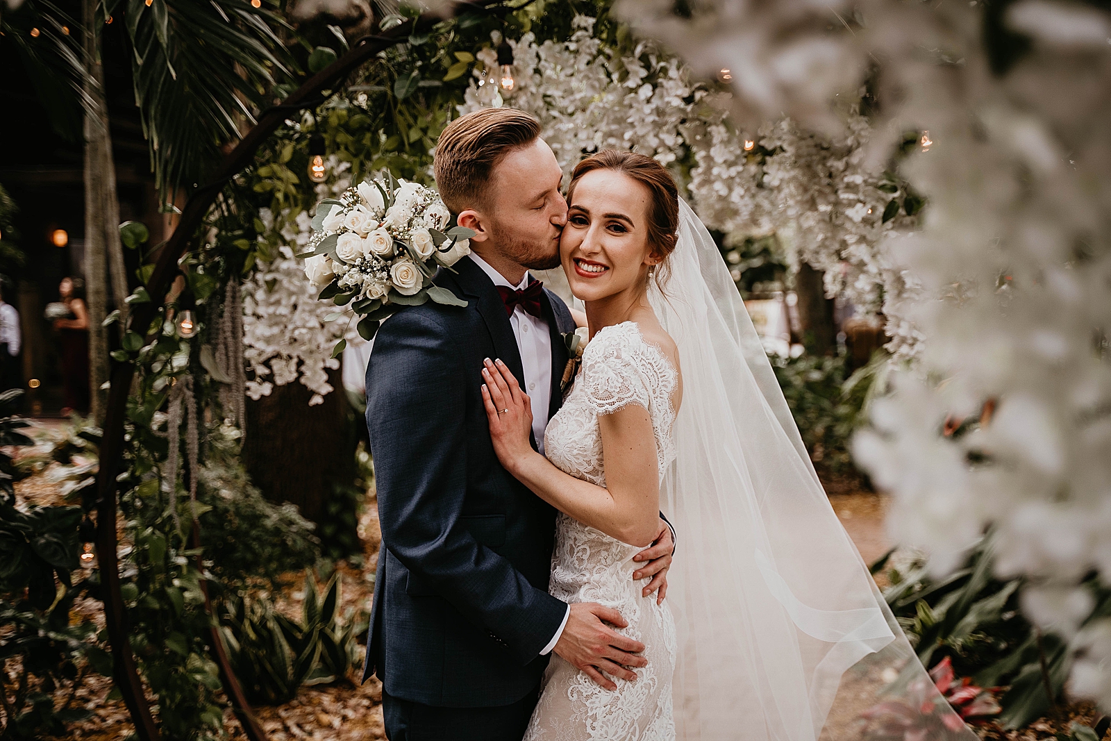 Groom kissing Bride on her cheek in garden area Living Sculptures Sanctuary Wedding Photography captured by South Florida Wedding Photographer Krystal Capone Photography 
