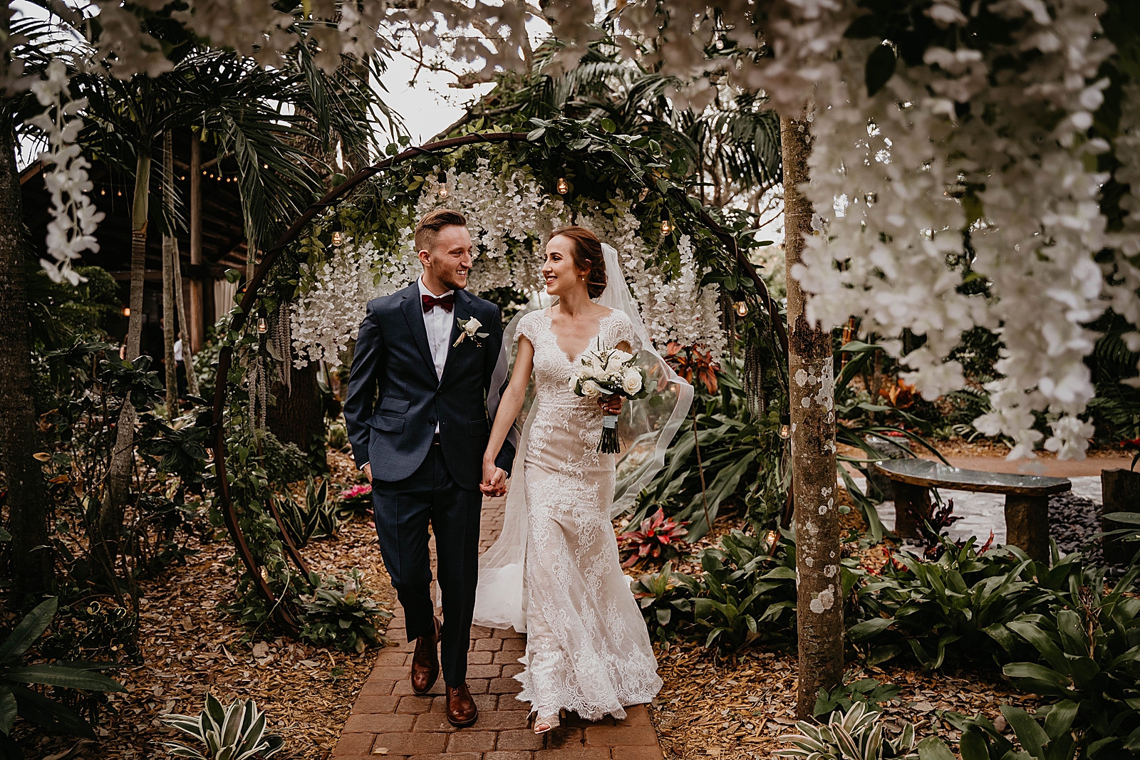Bride and Groom holding hands walking through botanical circular arch Living Sculptures Sanctuary Wedding Photography captured by South Florida Wedding Photographer Krystal Capone Photography 