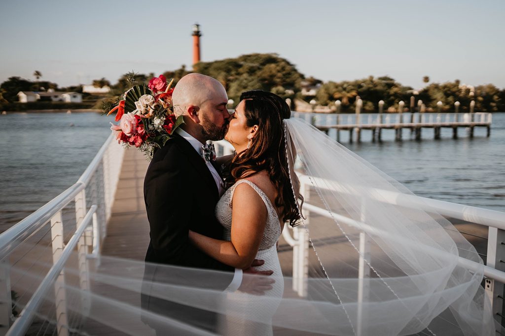 Bride and Groom kissing on dock with lighthouse in the background Pelican Club Wedding Photography captured by South Florida Wedding Photographer Krystal Capone Photography 