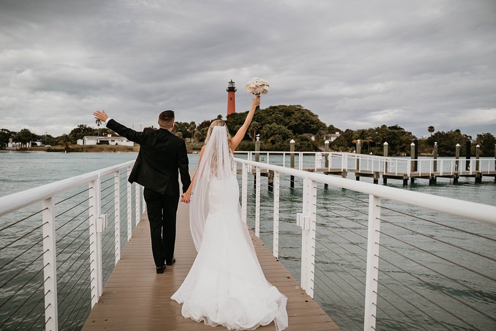 Bride and groom walking on dock with arms up in the air Pelican Club Wedding Photography captured by South Florida Wedding Photographer Krystal Capone Photography