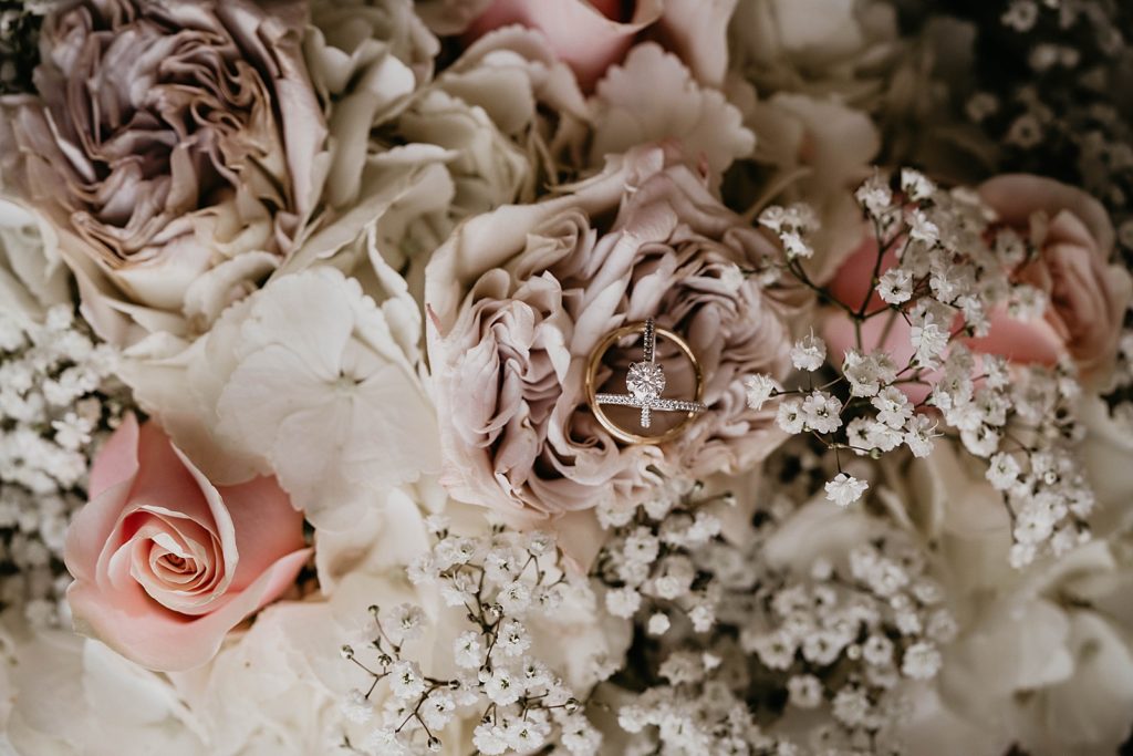 Detail shot of Bride's engagement ring and wedding bands on top of roses
