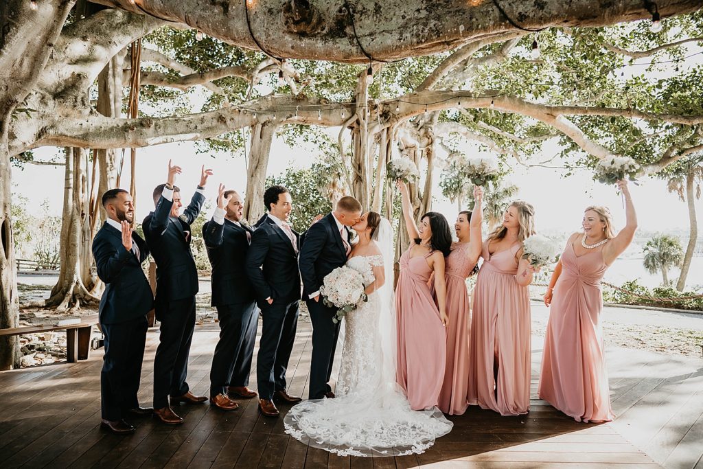 Bride and Groom kissing with wedding party celebrating